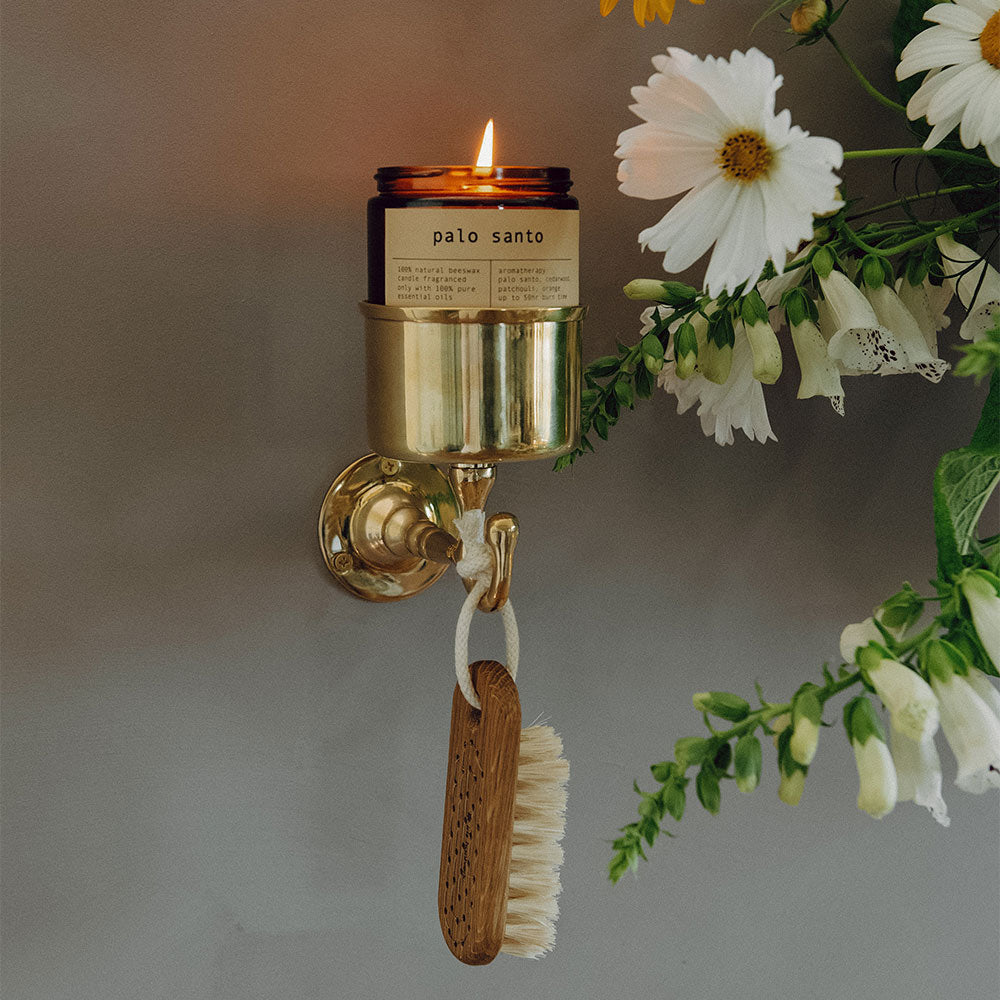Wall-mounted candle holder with a lit candle labeled 'palo santo' next to a bouquet of flowers.